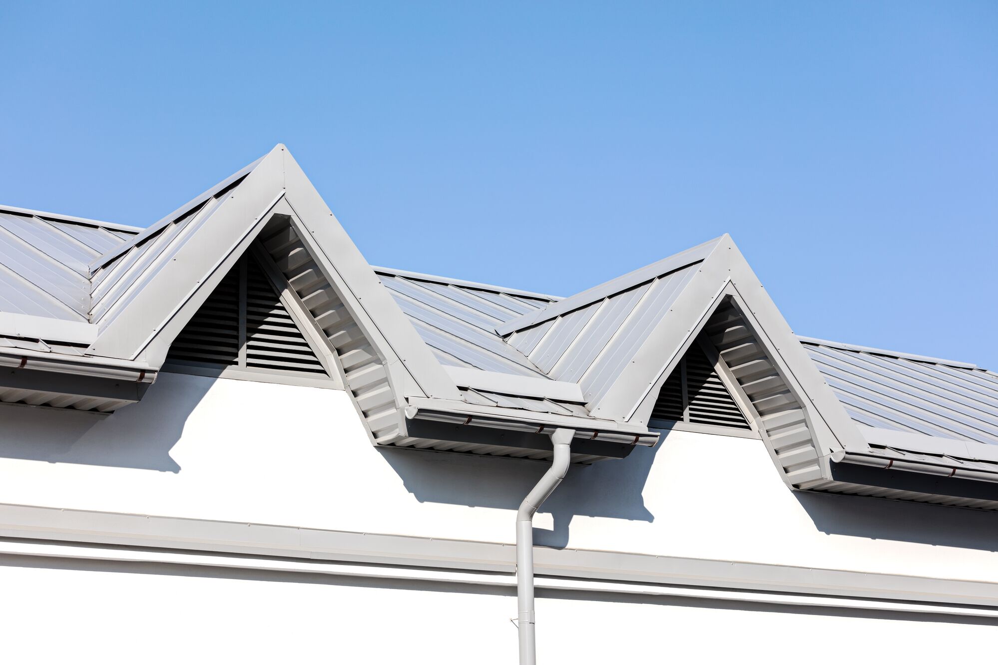 Metal roof peaks with a modern design against a clear blue sky, showcasing architectural features that enhance ventilation and aesthetics.
