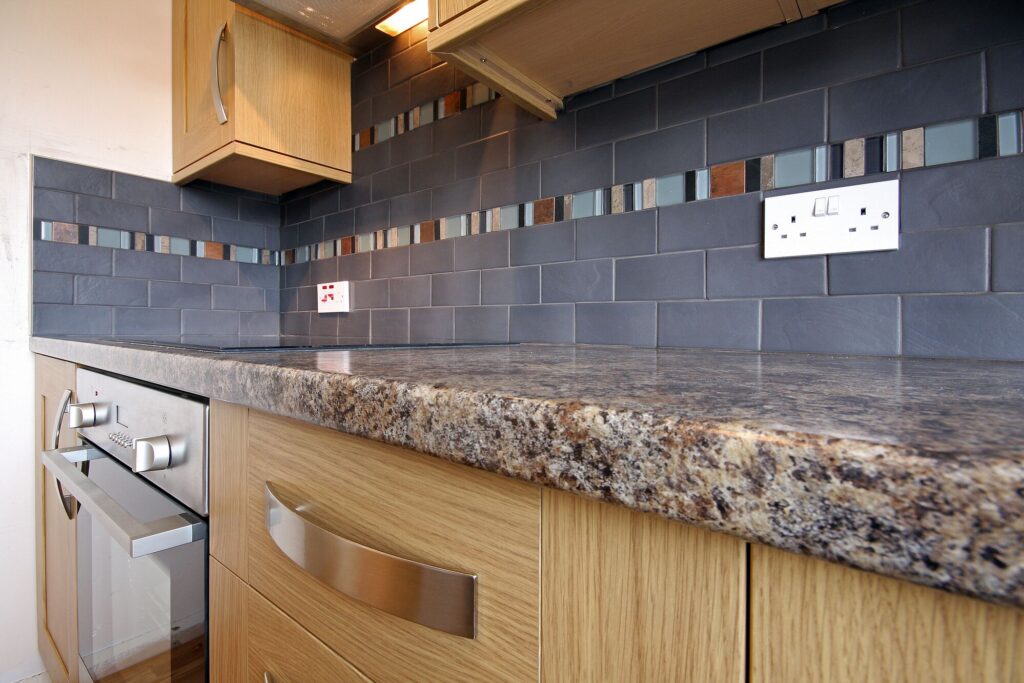 Modern kitchen featuring a granite countertop, wooden cabinetry, and a stylish tiled backsplash with colorful accents. Ideal for design inspiration.