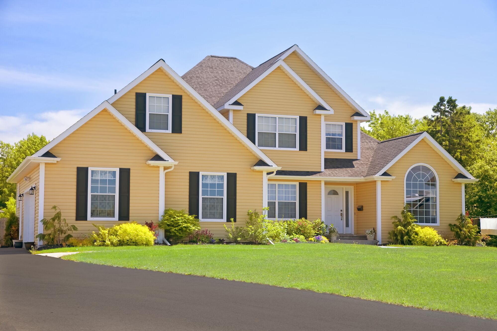 Two-story yellow house with green shutters and a well-maintained lawn. The bright exterior suggests a welcoming family home, ideal for real estate listings.