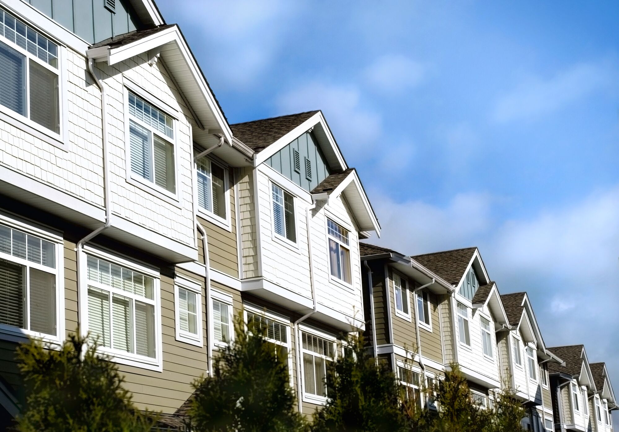 Stylish townhouses with varied architectural details, featuring large windows and pitched roofs under a clear blue sky. Ideal for urban living.