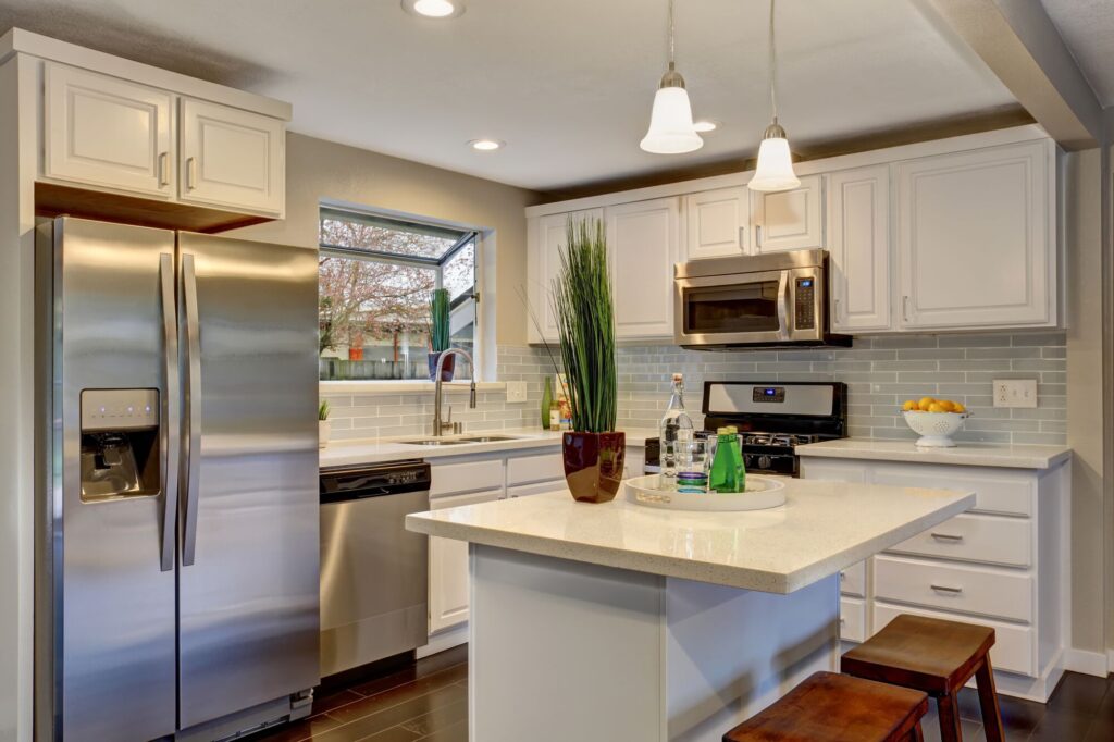 Modern kitchen featuring stainless steel appliances, white cabinetry, and a central island with a decorative tray. Natural light streams through the window.
