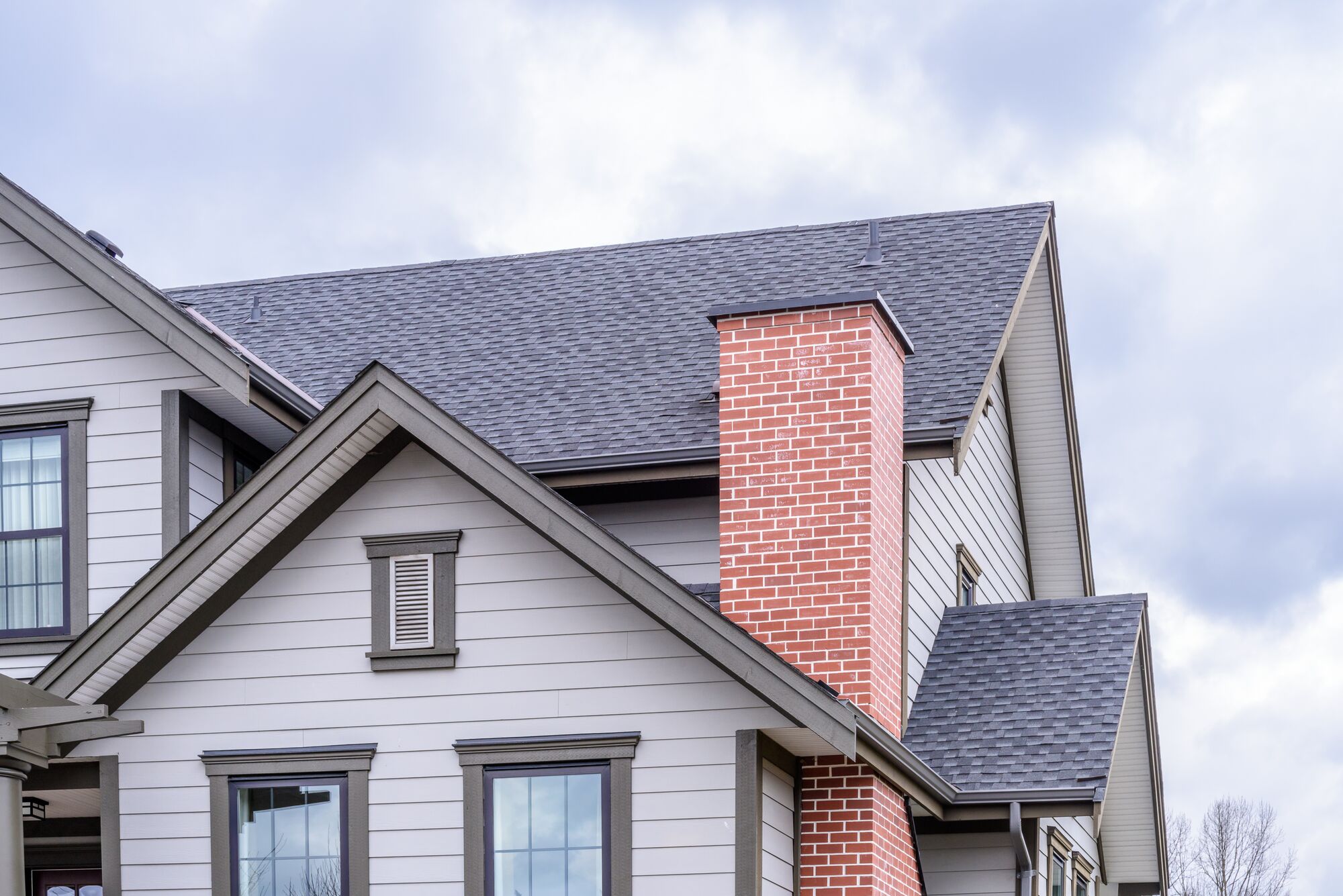 Stylish home exterior featuring a gray roof and a prominent red brick chimney, showcasing modern architectural design against a cloudy sky.