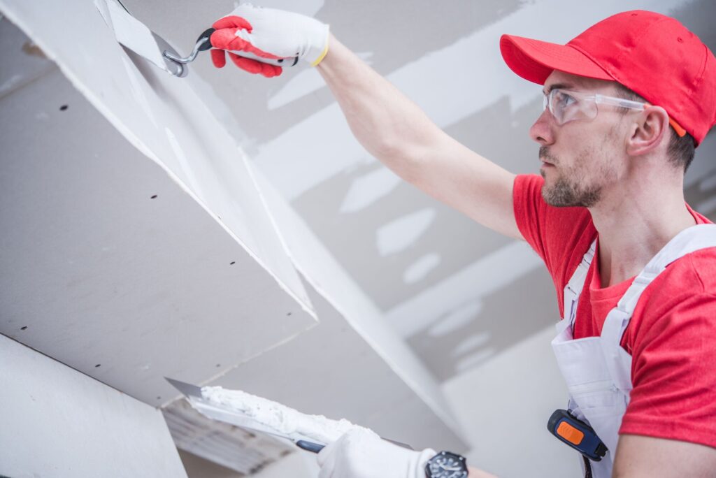 A construction worker applies joint compound to drywall while wearing gloves and safety goggles, showcasing home renovation techniques.